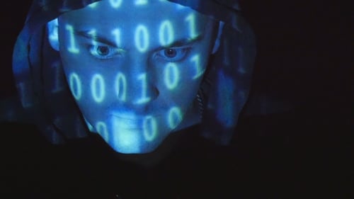 Hooded Hacker Working On a Computer, Binary Code Projecting On His Face. Source Code Projected Over