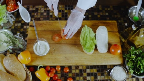 Gloved Hands Slicing Tomato to Prepare Sandwich