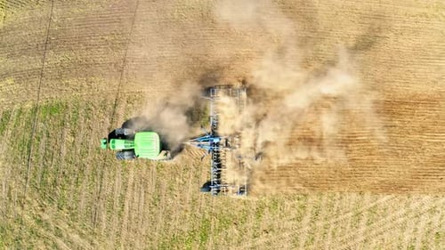 Aerial view of green tractor plowing dry field