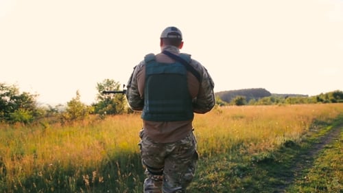 Soldier Walks with Rifle in Rural Field at Sunset