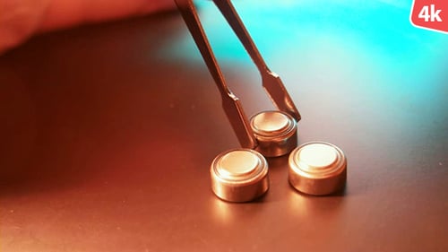 Button Cell Batteries Being Moved with Tweezers