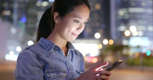 Femme envoyant un SMS sur un téléphone portable dans la ville la nuit