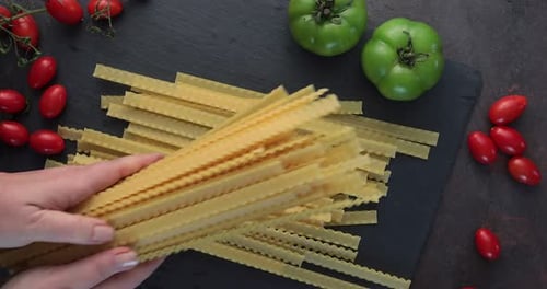Hands Preparing Pasta With Tomatoes on Dark Background