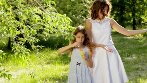 Beautiful Young Mother Together With Her Daughter In Nature Making Soap Bubbles