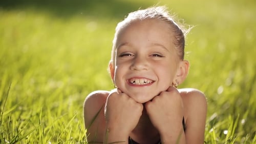 Little Girl At Sunset On The Grass And Smiling At Camera