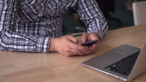 Man Using Smartphone at Desk with Laptop