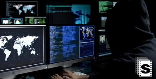 Hooded Hacker Typing at Multiple Computer Monitors