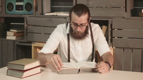Man With Beard Reads Book at Table