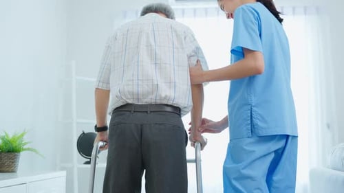 Nurse Helps Senior Man Walk with Walker Indoors