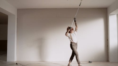 Young Adult Painting Ceiling with Roller in Unfurnished Room