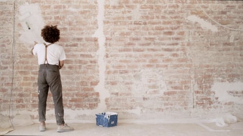 Young Adult Painting Brick Wall with White Paint