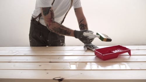 Man Varnishing Wooden Beams Indoors With a Brush