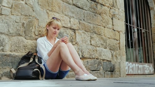Woman Sits and Uses Phone Against Stone Wall