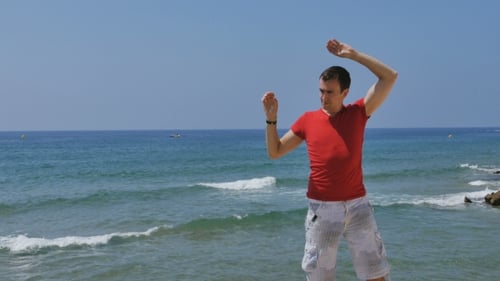 Man Stretches Arms at Ocean Beachfront on Sunny Day