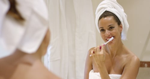 Woman Brushing Teeth in Bathroom Mirror