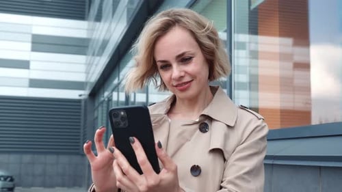 Woman Uses Smartphone Near Modern Building Exterior