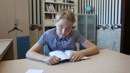 Boy Reads Book at Table Indoors