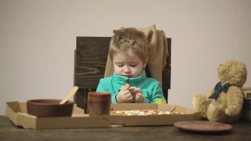 Serious Child Eats Pizza at Table Indoors