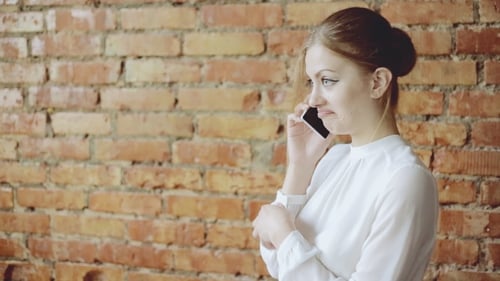 Woman Talks on Phone Against Brick Wall