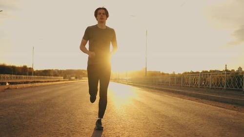 Yougn Athletic Man is Jogging Alone on Empty Road in Sunny Morning in Summer Sport Activity