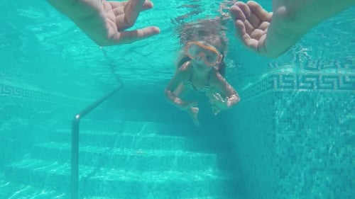 Child Swimming Underwater Approaching Hands in Pool