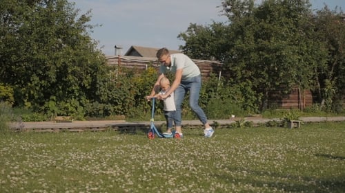 Father Helping Child Ride Scooter on Lawn