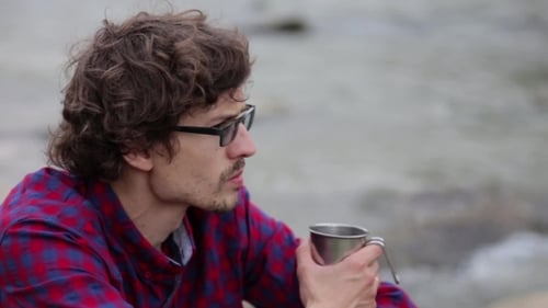 Young Man Drinking From Cup In Sunny Forest Near The Lake