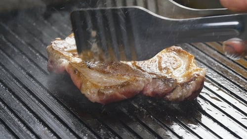 A Cook Turns Up a Steak Of Meat On a Grill In