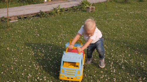 Blond Child Pulling Toy Truck on Grassy Lawn
