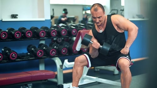 Chico culturista musculoso haciendo ejercicios con mancuernas en el gimnasio.
