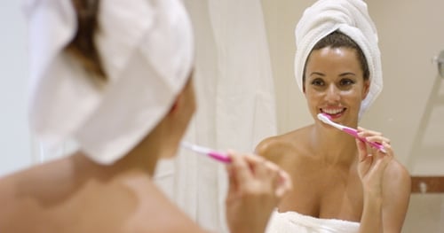 Woman Brushing Teeth in Bathroom Mirror