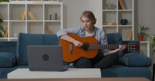 Mujer joven está viendo Vídeo tutorial y tocando la guitarra en casa Educación en línea Mujer principiante