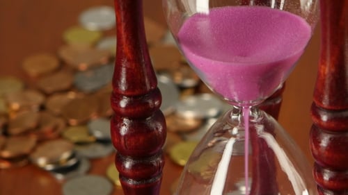 Hourglass On Coins Background.