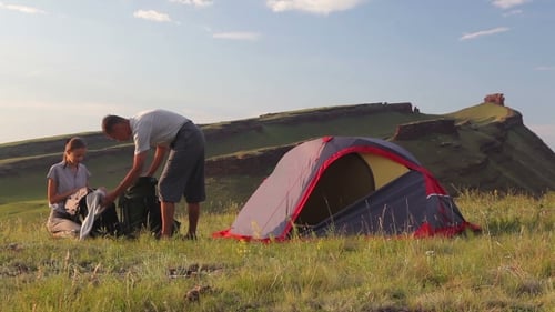Young Couple Prepares Backpacks And Rest In a Camp