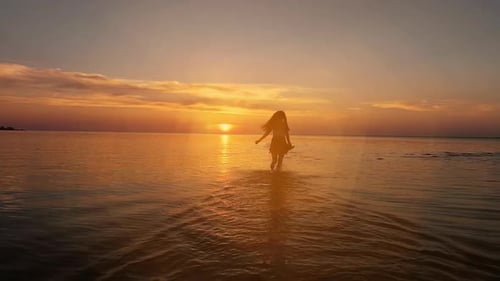 Brünette Frau in einem Kleid läuft bei Sonnenuntergang oder Sonnenaufgang am Wasser entlang