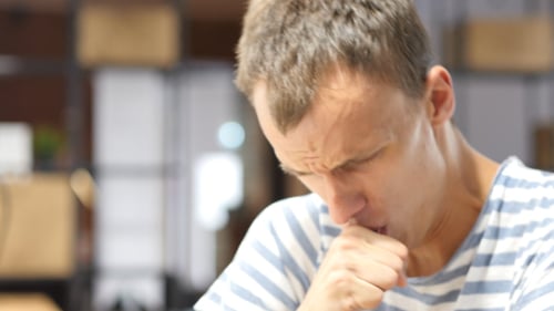 Young Adult Man Coughing into His Hand