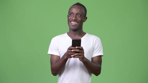 Young African Man Thinking While Using Phone Against Green Background