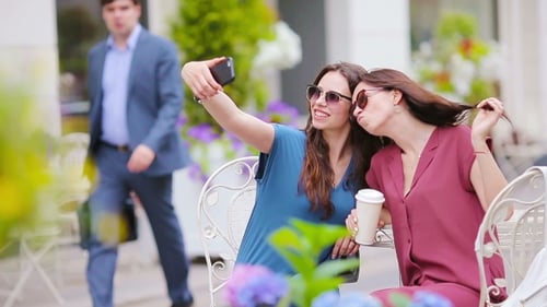 Two Young Girls Taking Selfie With Smart Phone At The Outdoors Cafe. Two Women After Shopping With