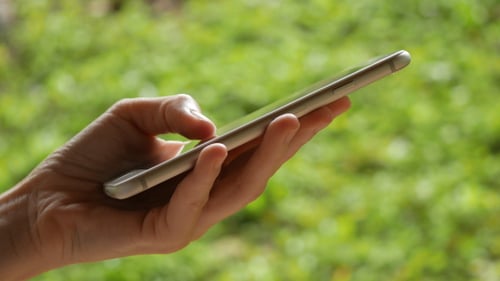 Hand Using Smartphone Outdoors with Green Background