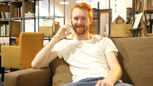 Red-Haired Man Talking on Phone, Relaxing on Sofa