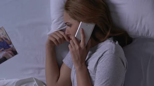 Weinende Frau im Bett schaut auf Familienfoto und ruft Ex-Ehemann an, Beziehungen