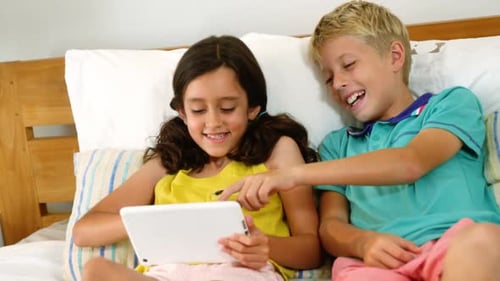 Children Laughing Together on Bed with Tablet