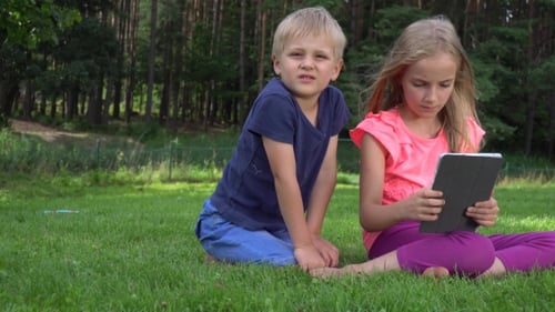 Children Using Tablet Together on Green Grass