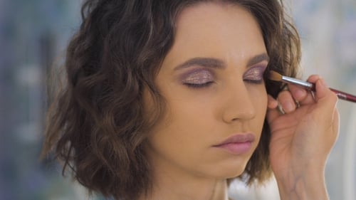 Maquilladora profesional aplicando maquillaje en un hermoso rostro joven para una sesión de fotos
