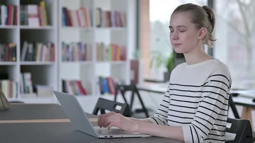 Laptop-Nutzung durch junge Frau, die in der Bibliothek in die Kamera lächelt