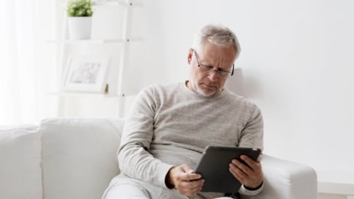 Senior Man Using Tablet Device on White Sofa