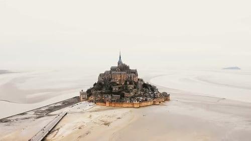Drone Flying Left Above Mont Saint Michel Island with Abbey and Road with Tourists During Low Tide