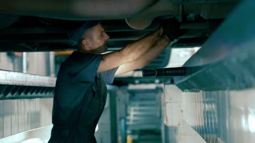 Mechanic Working Under Raised Car in Garage