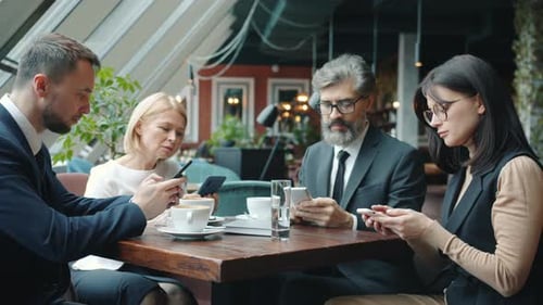 Group of Business Men and Women Using Smartphones Touching Screen at Table in Cafe