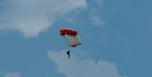 Skydiver Floating Down with Parachute in Cloudy Sky